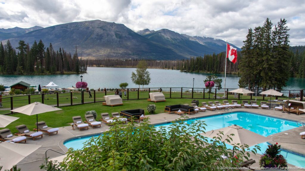 Outdoor pool with loungers and umbrellas overlooking Lac Beauvert and mountains at Jasper Park Lodge.