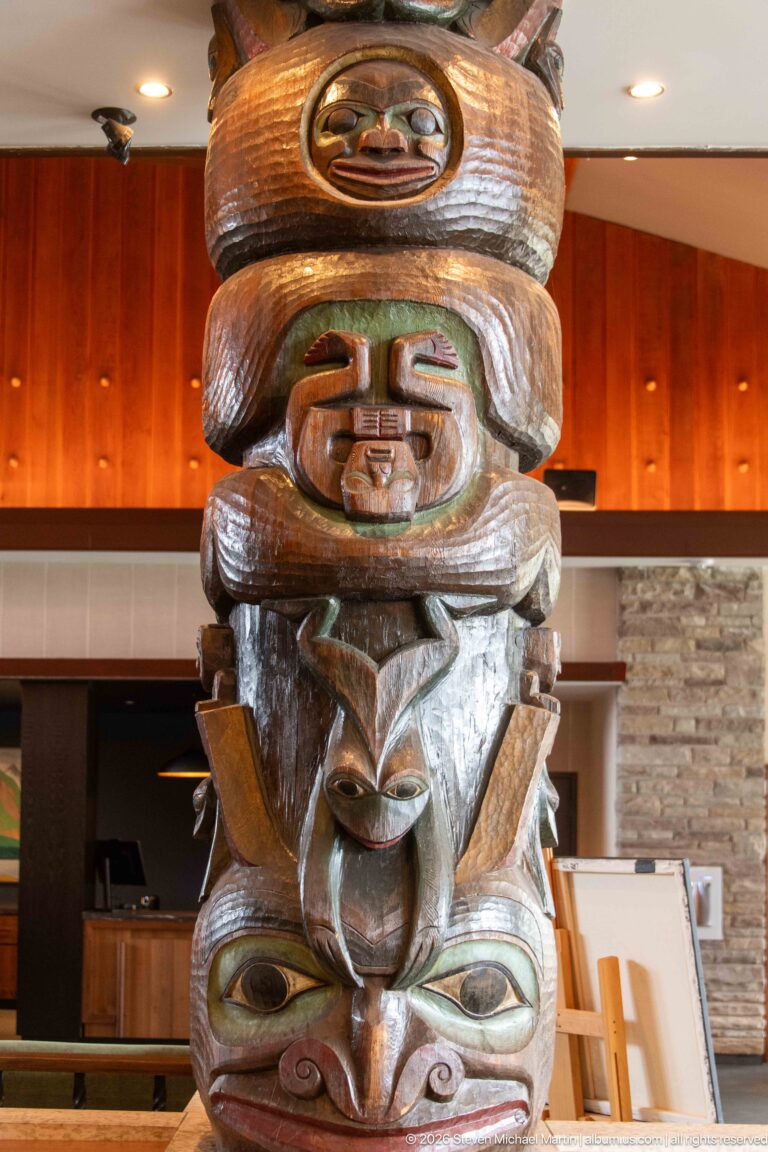Tall carved wooden column with stacked faces and animal-like forms inside Jasper Park Lodge.