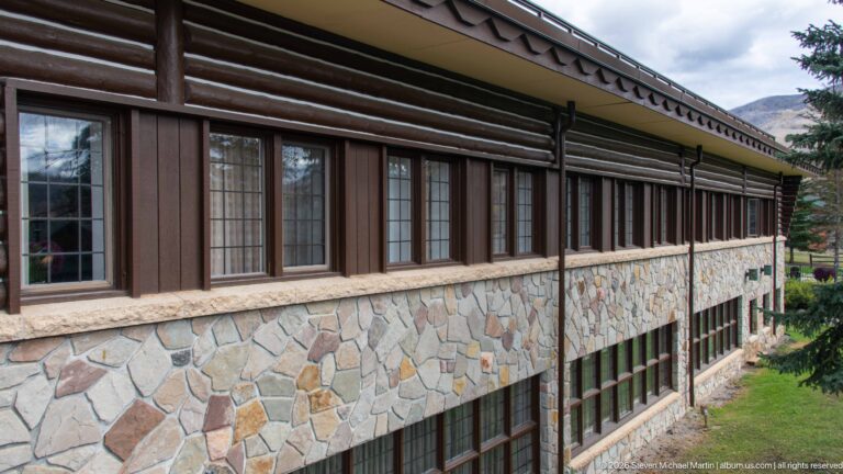 Oblique view of Jasper Park Lodge wall with multi-pane windows, dark timber siding, and stone masonry.