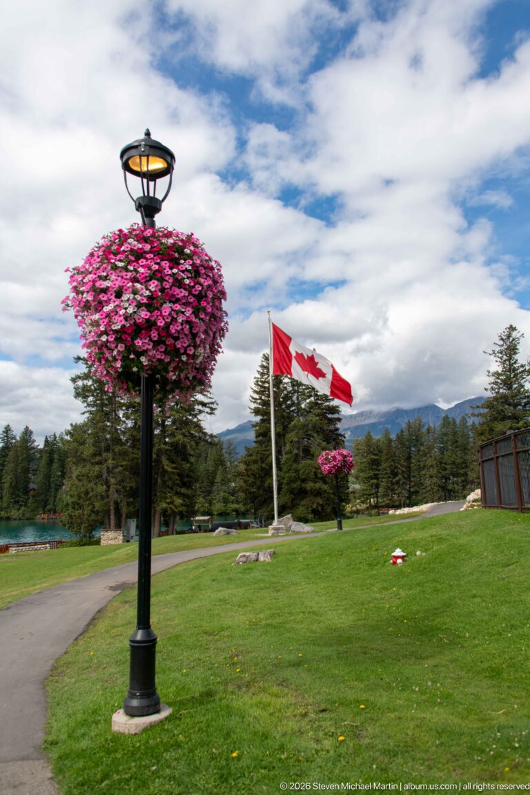 Canadian flag flying over Jasper Park Lodge grounds beside a large hanging basket of pink flowers.