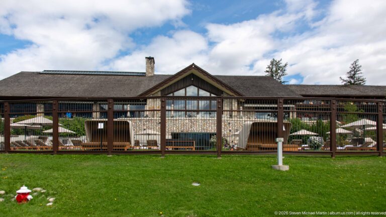 Long Jasper Park Lodge façade with central gable, terrace fencing, umbrellas, and green lawn.