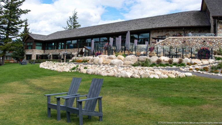 Two gray chairs on a lawn facing the stone-and-timber lakeside façade of Jasper Park Lodge.