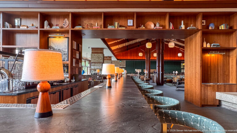 Long stone-topped lodge bar lined with lamps and patterned stools, with dining room beyond.