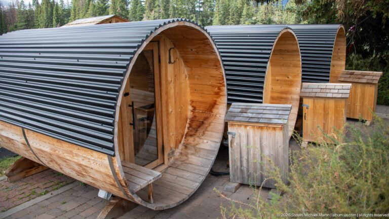 Three wooden barrel-shaped sauna units with dark curved roofs and open circular entrances.