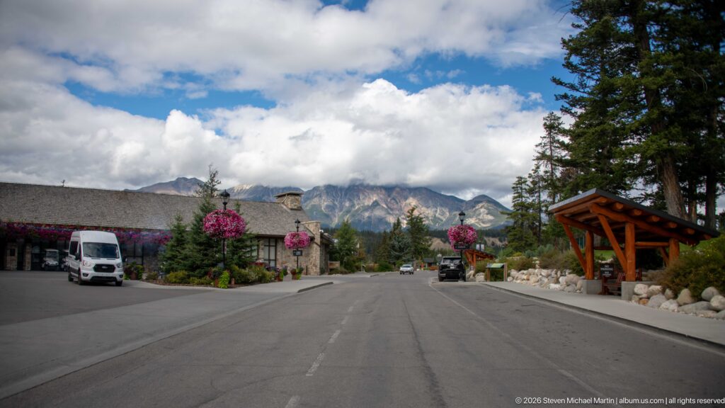 Road through Jasper Park Lodge buildings and flower baskets with mountains rising in the distance.