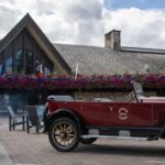 Burgundy open touring car with wood-spoked wheels parked outside the gabled Jasper Park Lodge entrance.