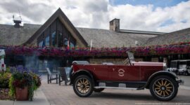 Burgundy open touring car with wood-spoked wheels parked outside the gabled Jasper Park Lodge entrance.