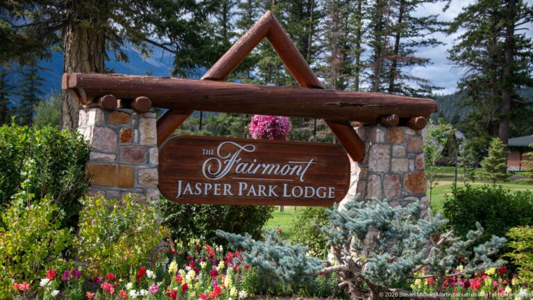 Timber and stone Fairmont Jasper Park Lodge sign surrounded by flowers and evergreen landscaping.