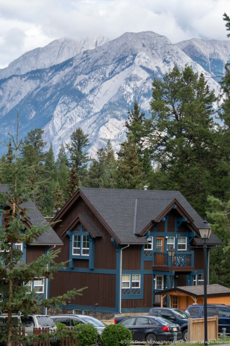 Brown multi-unit lodge building with blue trim and balconies below a pale mountain slope.
