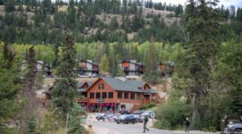 Rustic wood lodge buildings among trees above a road and parked cars near Pyramid Lake.