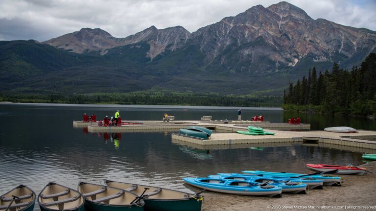 Canoes, blue kayaks, and floating docks on Pyramid Lake beneath a rugged mountain face.