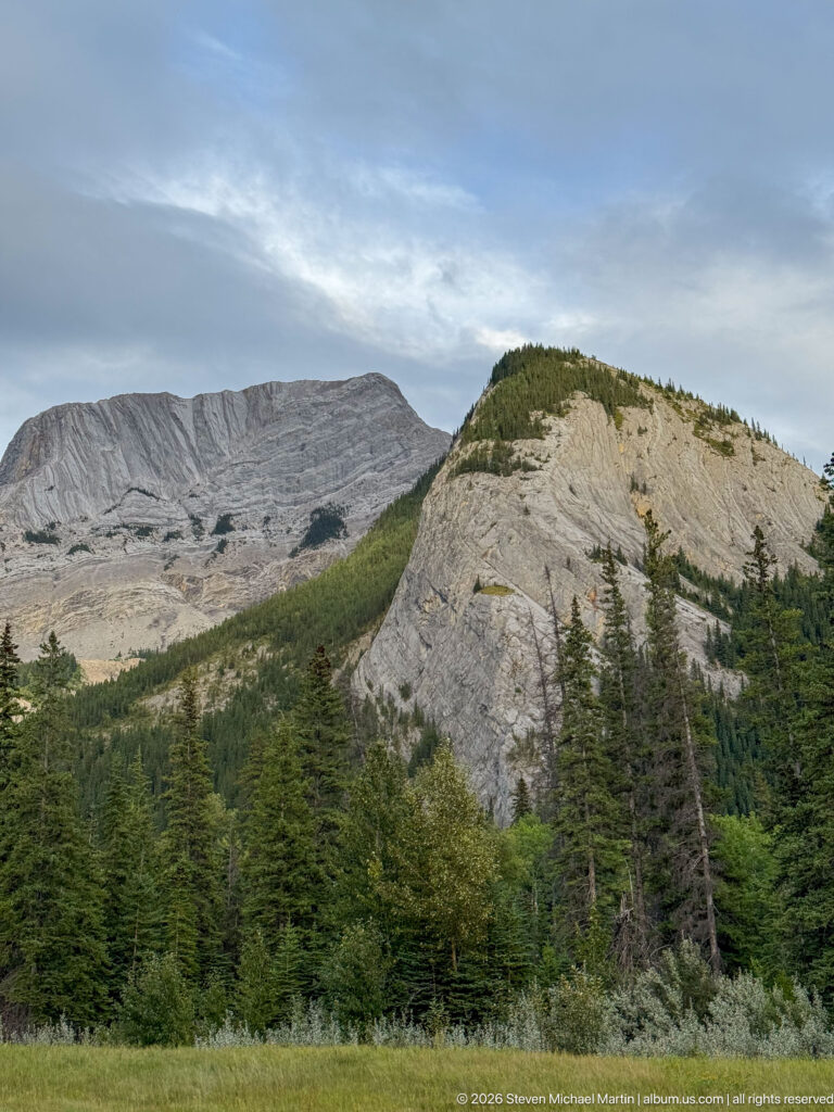Broad gray layered mountain ridge and rounded rock buttress above conifer forest near Pyramid Lake.