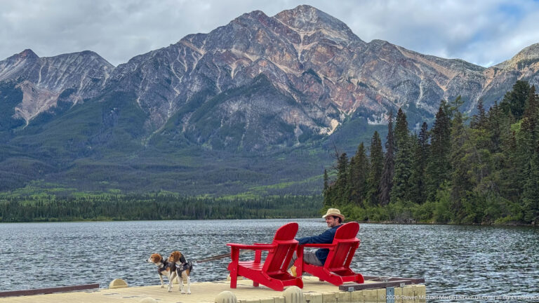 Visitor seated in a red chair beside a beagle on a dock, with Pyramid Lake and mountain behind.