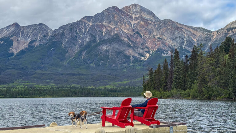 Visitor in a red chair with two beagles on a dock facing a massive mountain across Pyramid Lake.