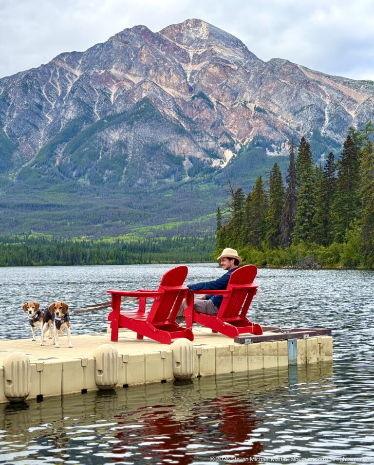 Two beagles and a seated visitor on a floating dock with a broad rocky mountain across Pyramid Lake.