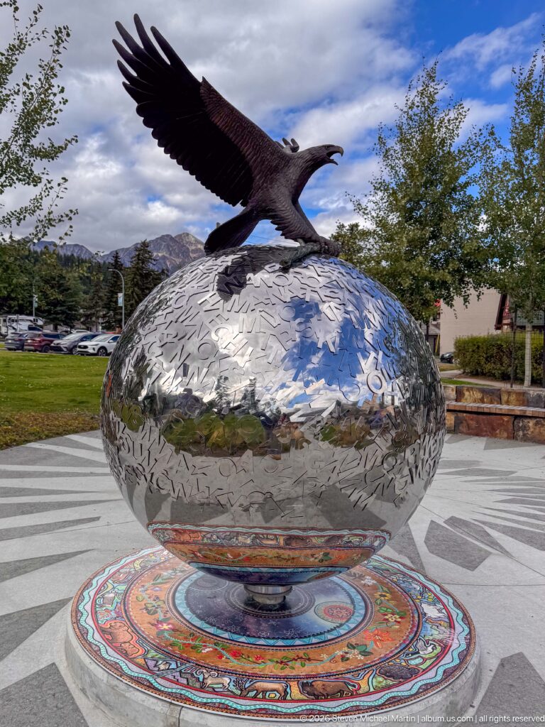 Dark metal eagle with outstretched wings perched on a reflective patterned globe above a colorful circular base.
