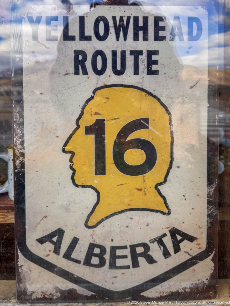 Weathered Yellowhead Route sign with a yellow profile-shaped shield, black route number 16, and Alberta lettering.