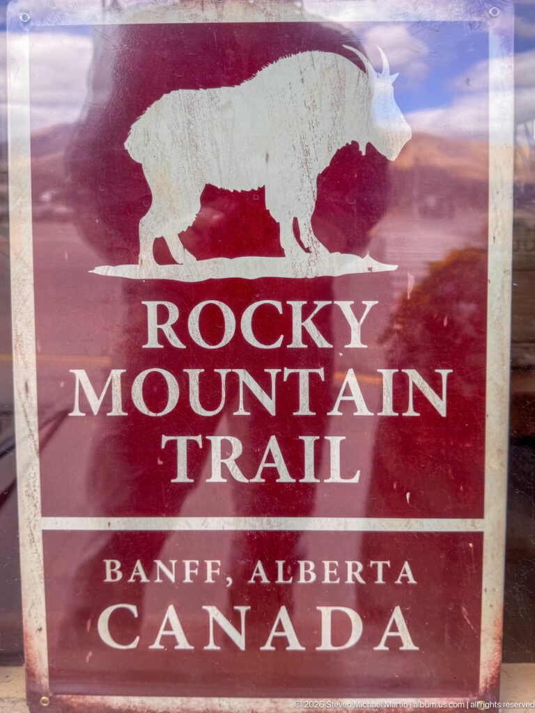 Weathered red Rocky Mountain Trail sign with a white bison silhouette and Banff, Alberta, Canada lettering.
