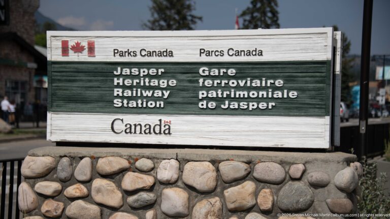 Weathered bilingual Parks Canada sign for Jasper Heritage Railway Station mounted on a rounded-stone base.