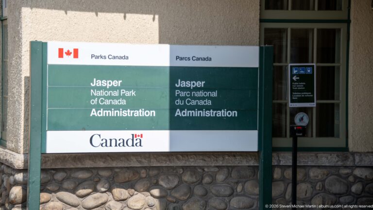 Bilingual Parks Canada sign reading Jasper National Park of Canada Administration beside a fieldstone wall and green-trimmed window.