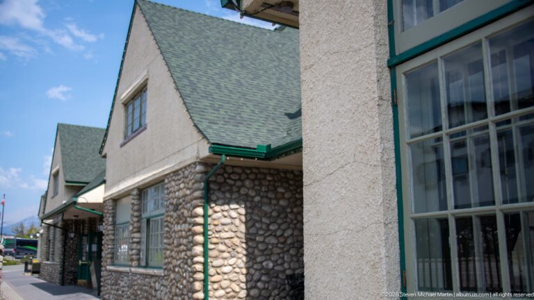 Oblique exterior detail of Jasper railway station showing fieldstone masonry, stucco walls, green trim, windows, and shingled roofs.
