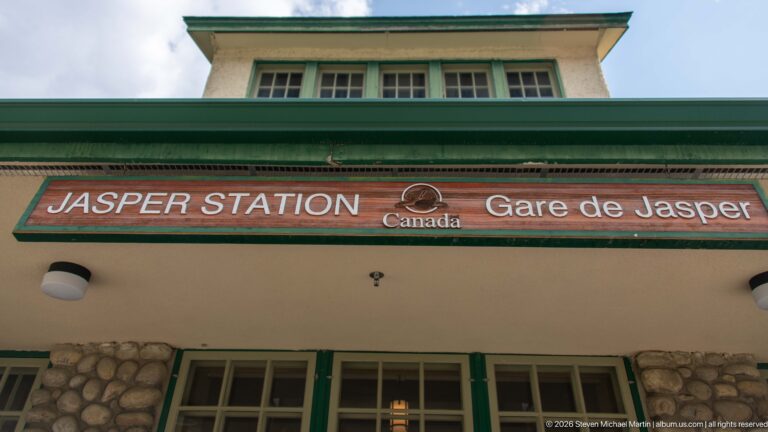Bilingual Jasper Station and Gare de Jasper sign above green-trimmed windows and a rounded fieldstone wall base.