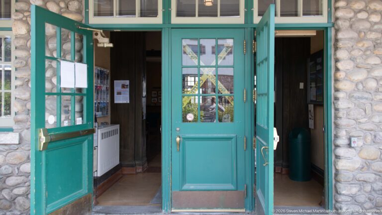 Open green glazed double doors with brass-colored hardware set between fieldstone walls at Jasper railway station.