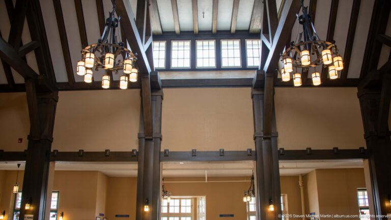 Tall timber posts, clerestory windows, exposed ceiling beams, and clustered chandeliers inside Jasper railway station.