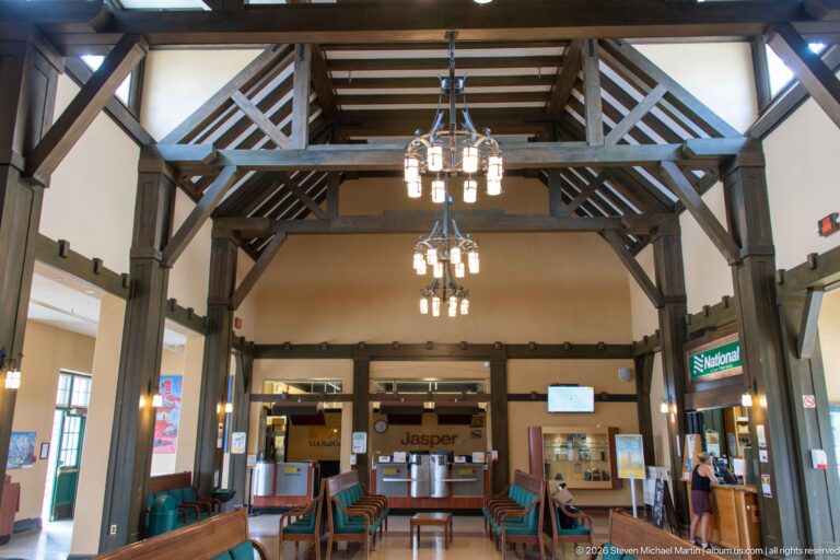 Jasper station interior with triangular timber roof bracing, chandeliers, waiting-room seating, and ticket counters below.