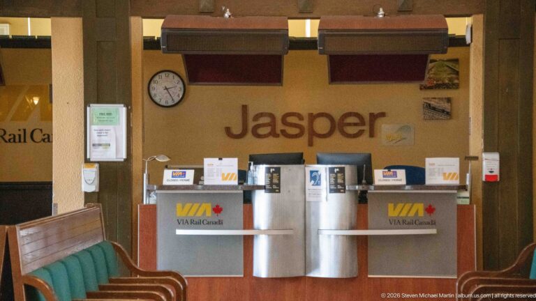 Two VIA Rail Canada counters beneath large Jasper lettering, with a wall clock, monitors, notices, and wooden seating.