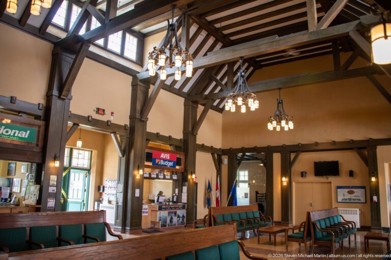 Timber-framed Jasper station interior with chandeliers, green benches, rental counters, service desks, and commercial signs.
