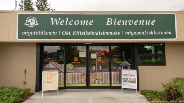 Visitor-centre entrance with green multilingual Welcome and Bienvenue sign above glass doors and event posters.