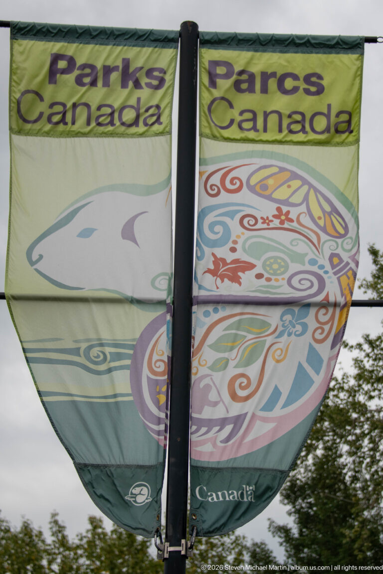 Green and cream Parks Canada fabric banner with a large colorful stylized animal motif hanging from a vertical pole.