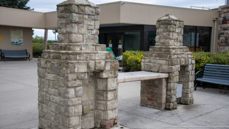 Two stepped rough-stone piers joined by a low stone bench in the paved plaza outside the visitor centre.