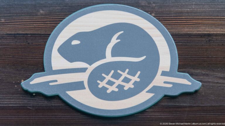 Round blue-gray and cream emblem showing a stylized beaver above water, mounted on dark wooden boards.