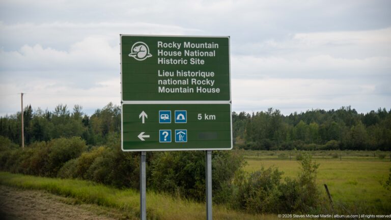 Green bilingual highway sign for Rocky Mountain House National Historic Site with five-kilometre distance and service symbols.