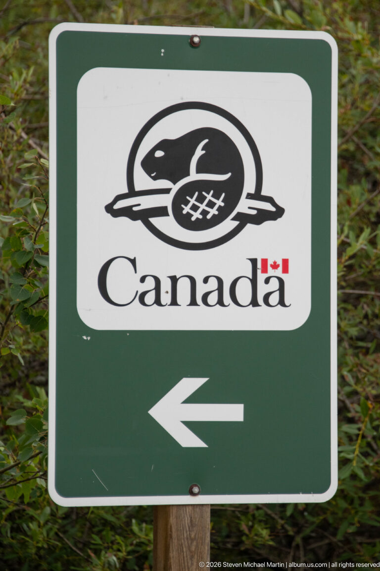 Green Parks Canada directional sign with black-and-white beaver emblem, Canada wordmark, and white arrow pointing left.