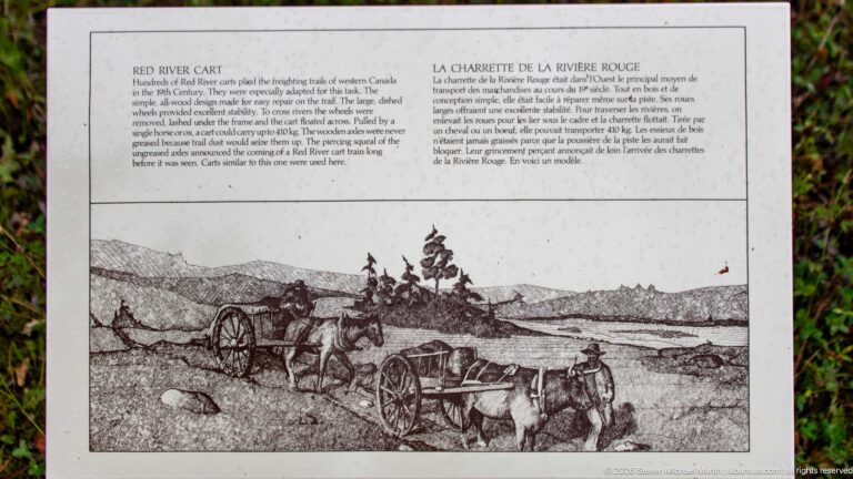 Bilingual interpretive panel with historical drawing of horse-drawn two-wheeled Red River carts crossing open prairie.