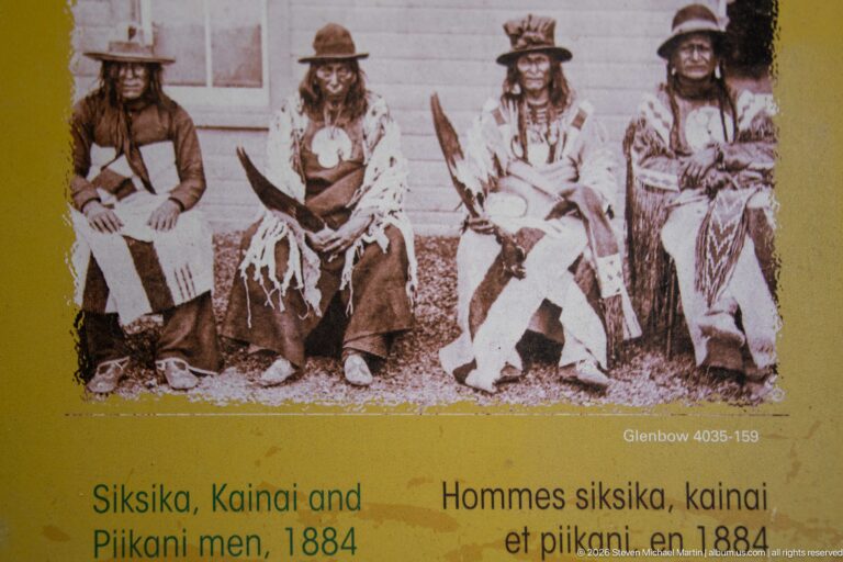 Reproduced 1884 archival portrait of four seated Siksika, Kainai and Piikani men in varied clothing and hats.