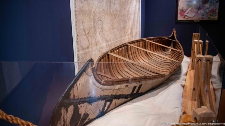 Close view into a bark-covered watercraft showing closely spaced wooden ribs, longitudinal members, and an upturned pointed end.