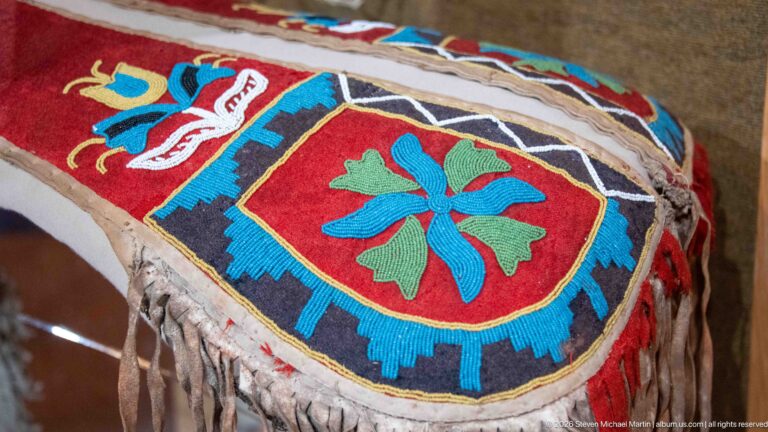 Close detail of colorful floral and geometric beadwork on a fringed hide or leather object.