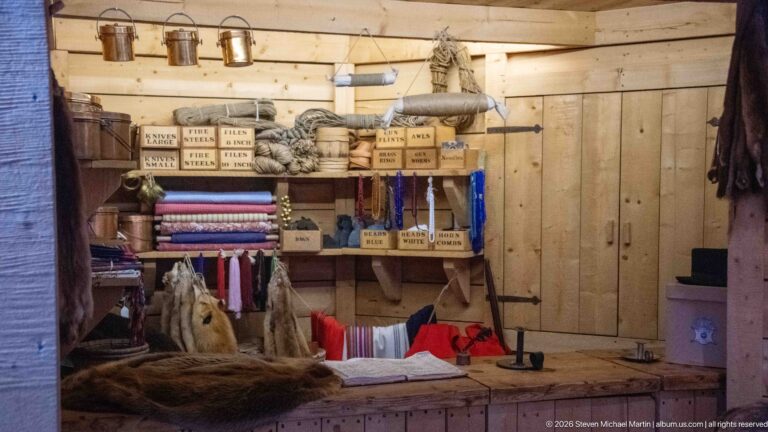 Recreated wooden trading-post counter stocked with folded textiles, boxes, rope, and assorted goods.
