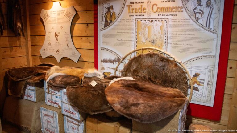 Several brown animal pelts displayed over boxes beneath a trade and commerce interpretive panel.