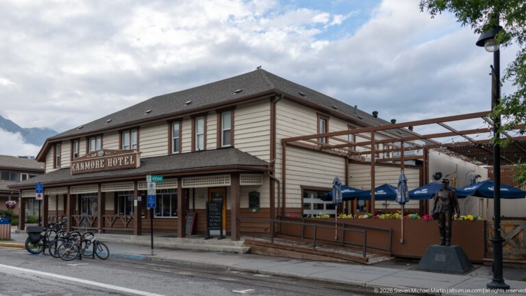 A side view of the Canmore Hotel shows its patio, bicycles, and a dark figure on a plinth.