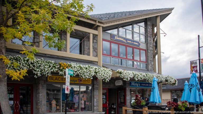 Glacier Lodge’s stone-and-timber façade rises above shops lined with white flower baskets.