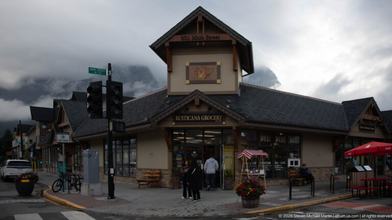 A grocery storefront with a tall central gable stands beneath low mountain clouds.