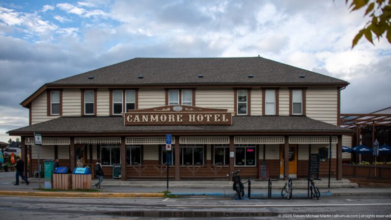 The Canmore Hotel’s two-story façade faces a wet street, with bicycles parked outside.