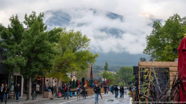 A pedestrian avenue with scattered visitors descends toward mountains hidden by mist.