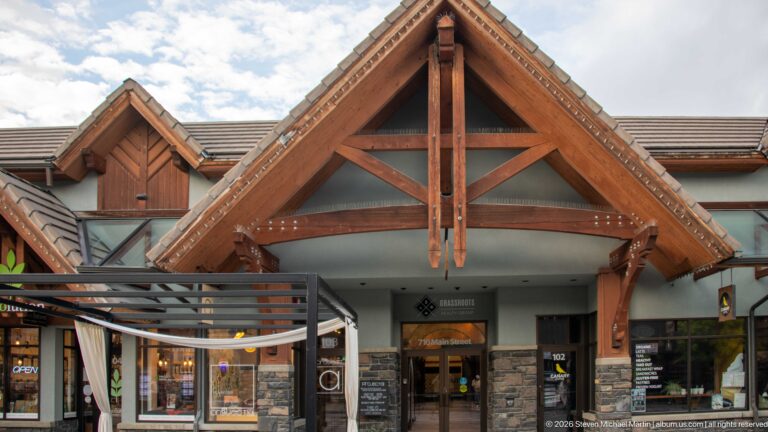 An exposed timber truss canopy projects above a stone-clad shop entrance and adjoining gabled storefronts.
