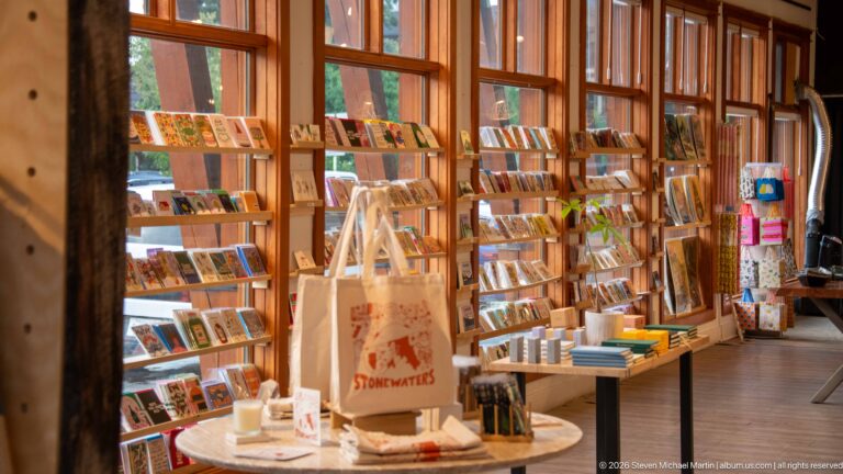 Books, postcards, prints, and gifts fill a warmly lit shop with tall timber-framed windows.